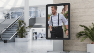 LED Display zeigt digitale Werbung in einem modernen Einkaufszentrum neben einer Rolltreppe und grünen Pflanzen.