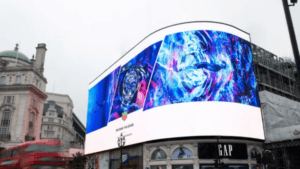 Großes gebogenes LED-Display mit bunter Uhrenwerbung über einem GAP-Geschäft in der Stadt.
